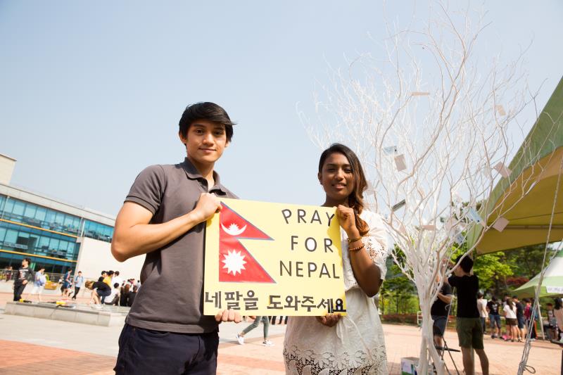 Luc Loja (left) and Cerian Vaidya (right) of the UNIST International Student Organization (UISO), holding a sign that said "Pray for Nepal" on Saturday near the Student Union Building to raise funds to support the victims and send aid to Nepal.