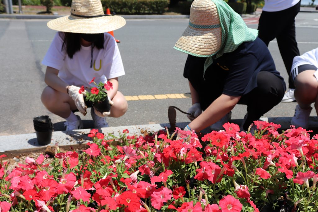 Participants are planting flowers in designated landscaping beds near the symbolic landmark of UNIST. l Image Credit: UNIST Leadership Center