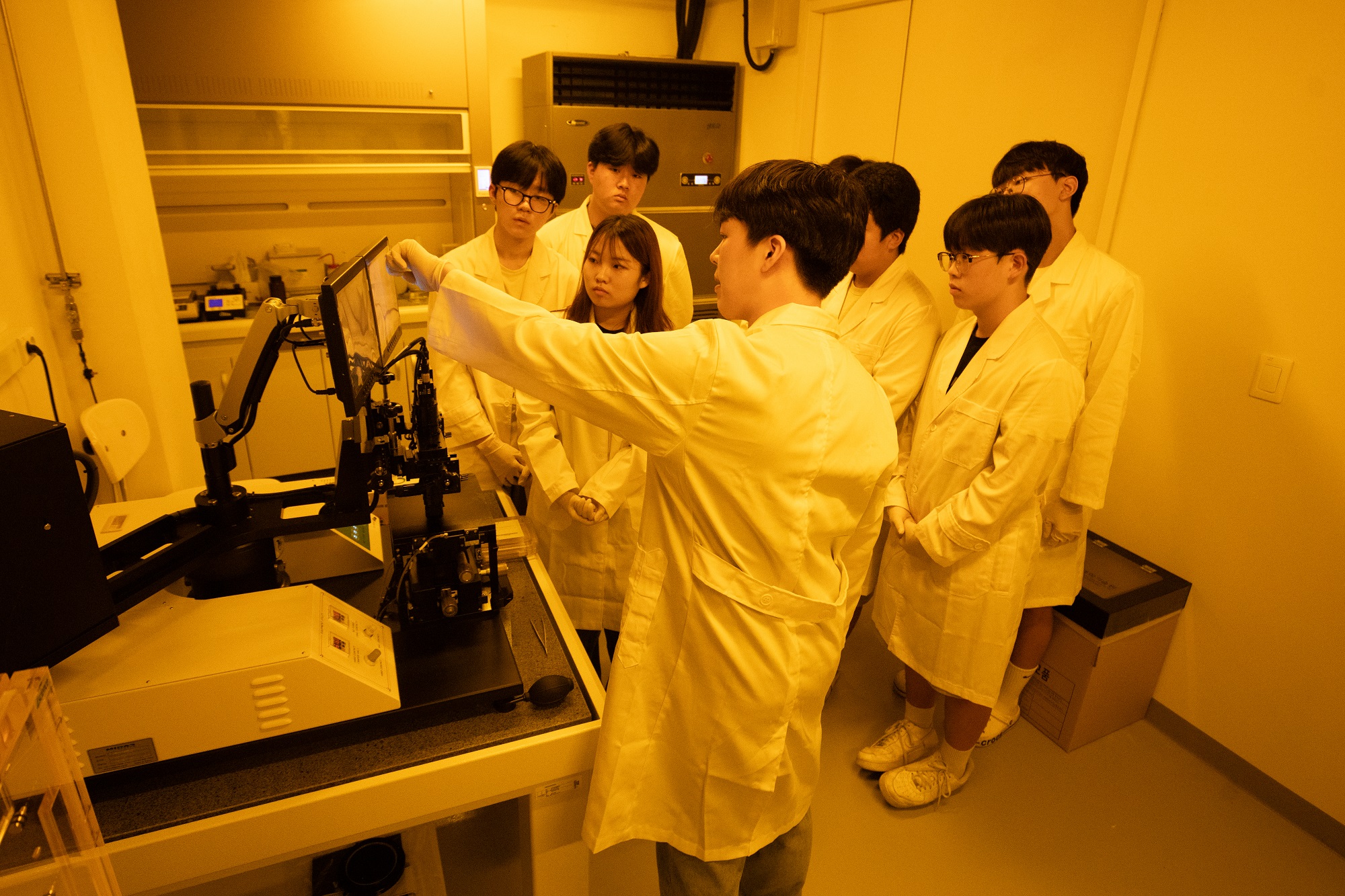 Youth participating in the program are wearing lab coats and experiencing photolithography experiments.